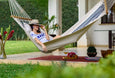 Navy and natural cotton hammock gently swaying on a sunlit patio, styled with pillows and surrounded by Mediterranean greenery. Mari Tefel, the creative designer, on the picture too.