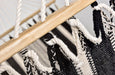Handwoven black and natural cotton hammock with wooden spreader bar, displayed outdoors on a hammock stand — artisan-crafted for luxury lounging.
