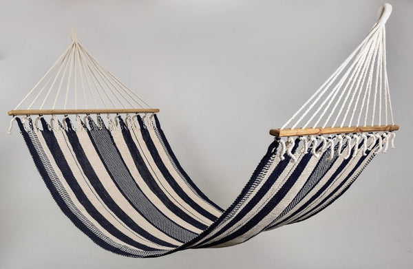Handwoven black and natural cotton hammock with wooden spreader bar, displayed outdoors on a hammock stand — artisan-crafted for luxury lounging.