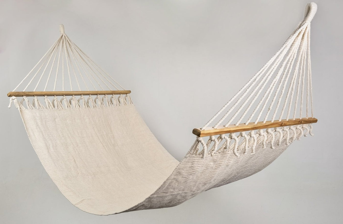 Luxury cotton hammock with wooden bar, styled outdoors with soft shadows and boho decor.